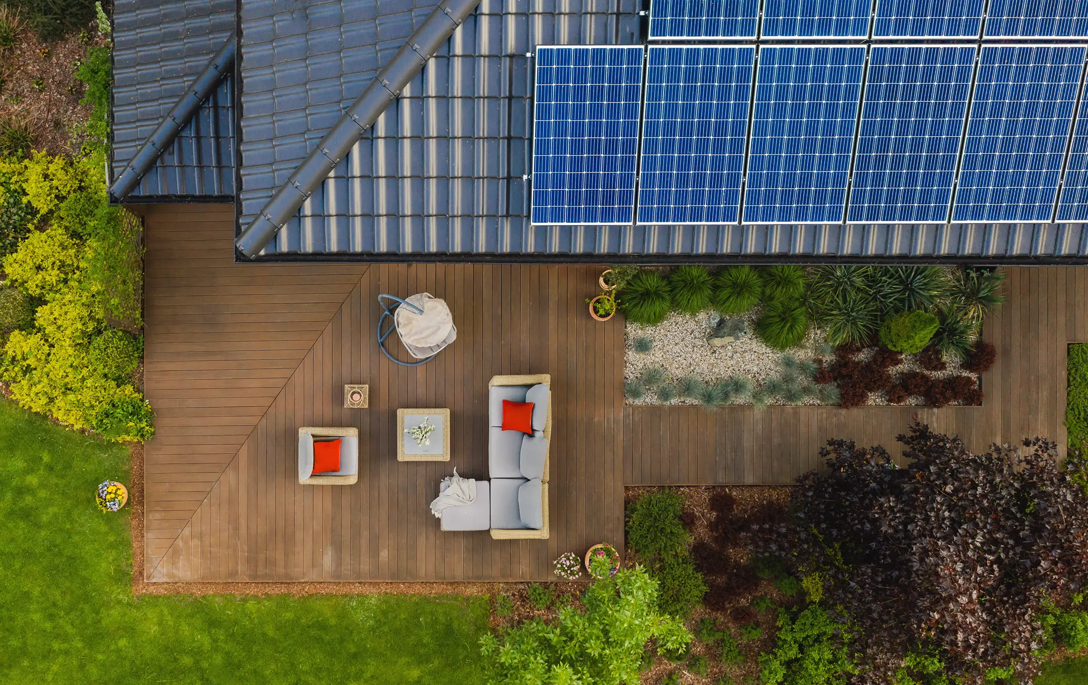 Luftaufnahme eines Einfamilienhauses mit großer Solaranlage auf dem Dach und moderner Holzterrasse