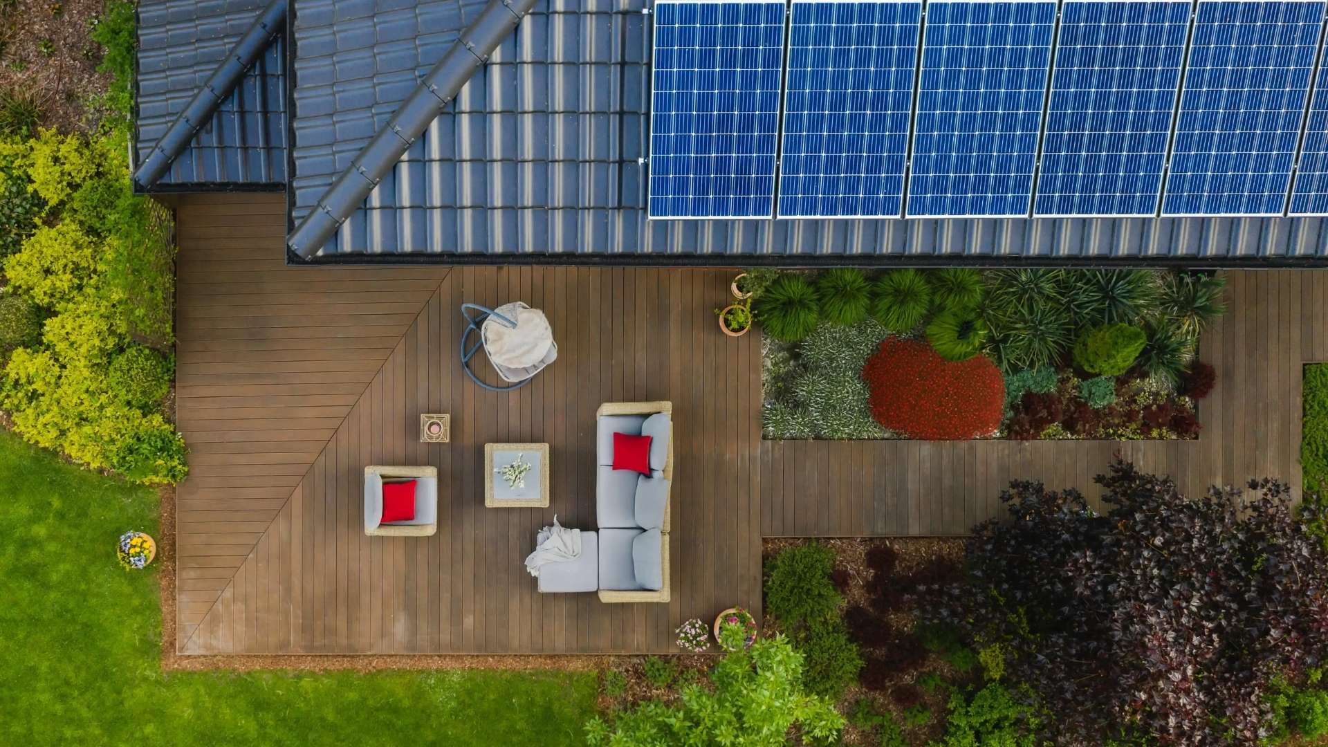 Luftaufnahme eines Einfamilienhauses mit großer Solaranlage auf dem Dach und moderner Holzterrasse